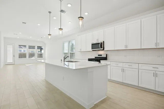 a kitchen with stainless steel appliances granite countertop a stove top oven a sink a refrigerator and white cabinets with wooden floor