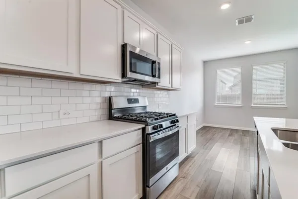 a kitchen with stainless steel appliances white cabinets granite counter tops and a window