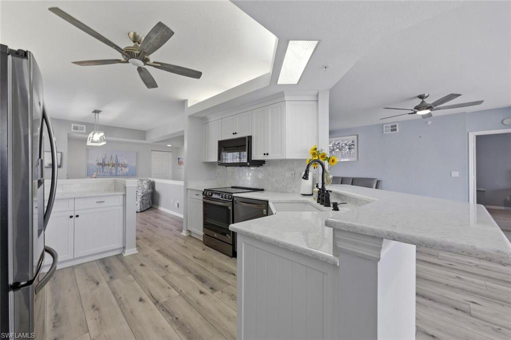 6899 Rain Lily Road, Unit 103 Naples, FL 34109 - Photo 11 of 39 Kitchen with a ceiling fan, a peninsula, white cabinets, stainless steel appliances, and light wood-type flooring
