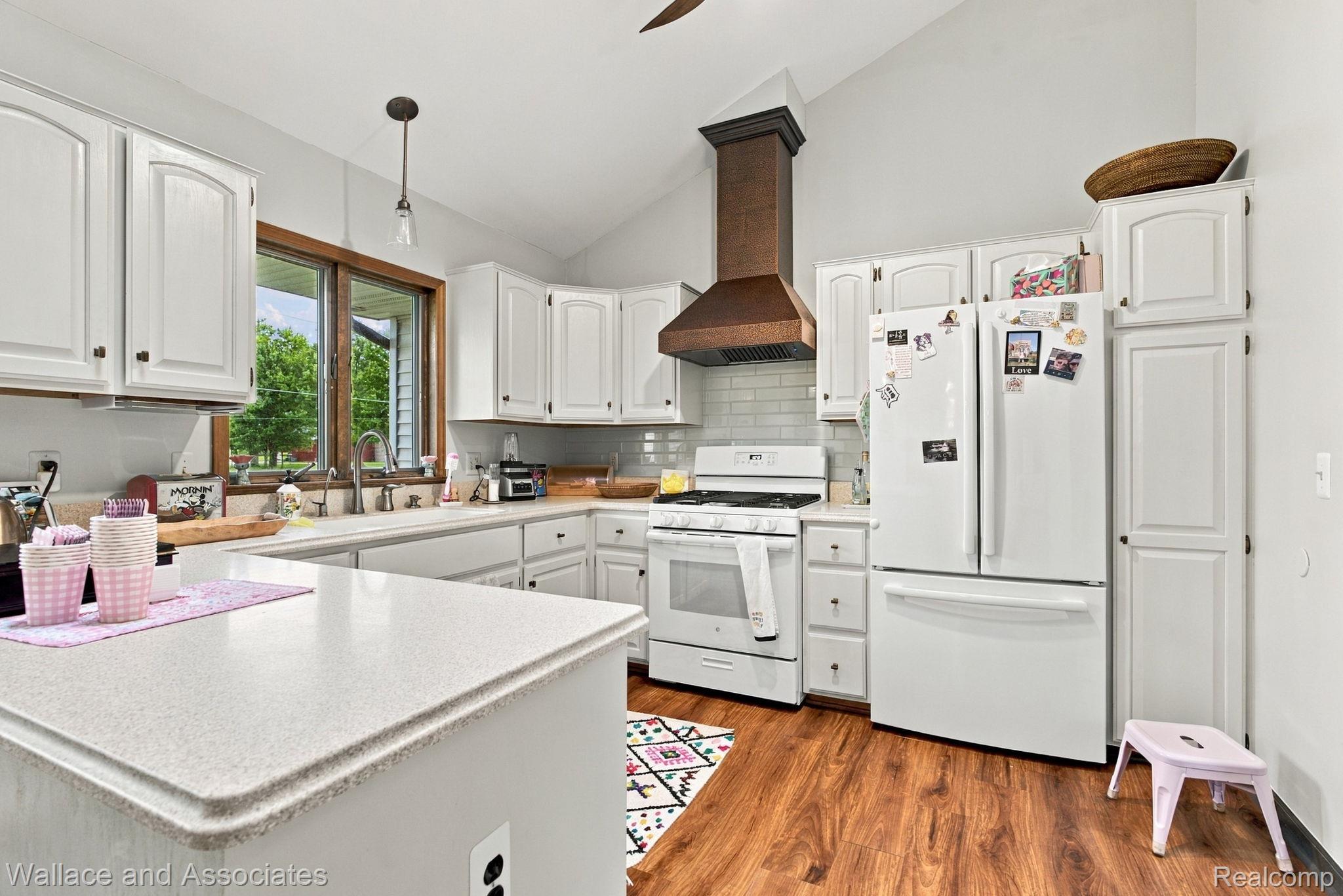 17076 27 Mile Road Ray, MI 48096 - Photo 15 of 63 Kitchen featuring vaulted ceilings, white cabinetry, a copper-tone range hood, white appliances, and wood-finish flooring