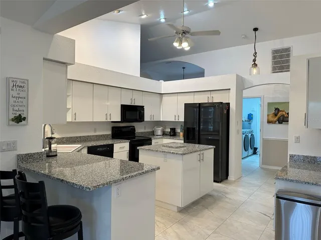 a kitchen with stainless steel appliances kitchen island granite countertop a refrigerator oven a sink dishwasher and white cabinets with wooden floor