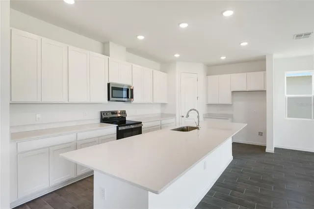 a kitchen with stainless steel appliances a sink a stove a microwave a center island and cabinets