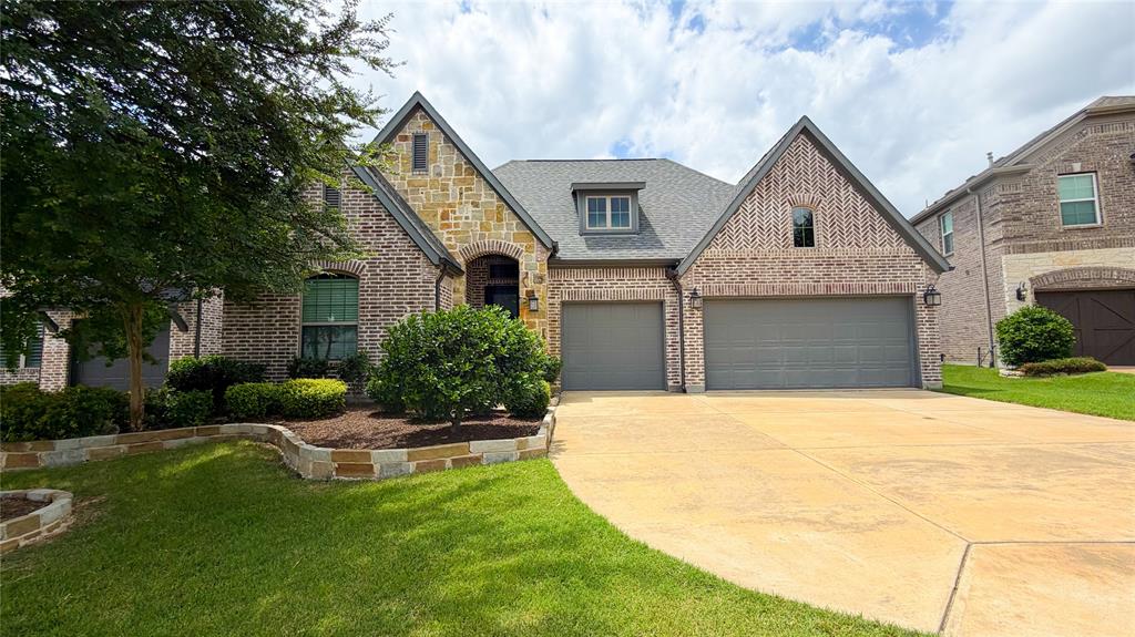 3201 Calvin Road McKinney, TX 75071 - Photo 3 of 11 Brick and stone facade residence featuring a two-car garage with gray doors, a gabled roofline, and dormer windows