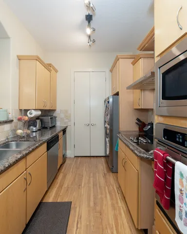 a kitchen with stainless steel appliances a stove top oven a sink a refrigerator wooden floor and cabinets