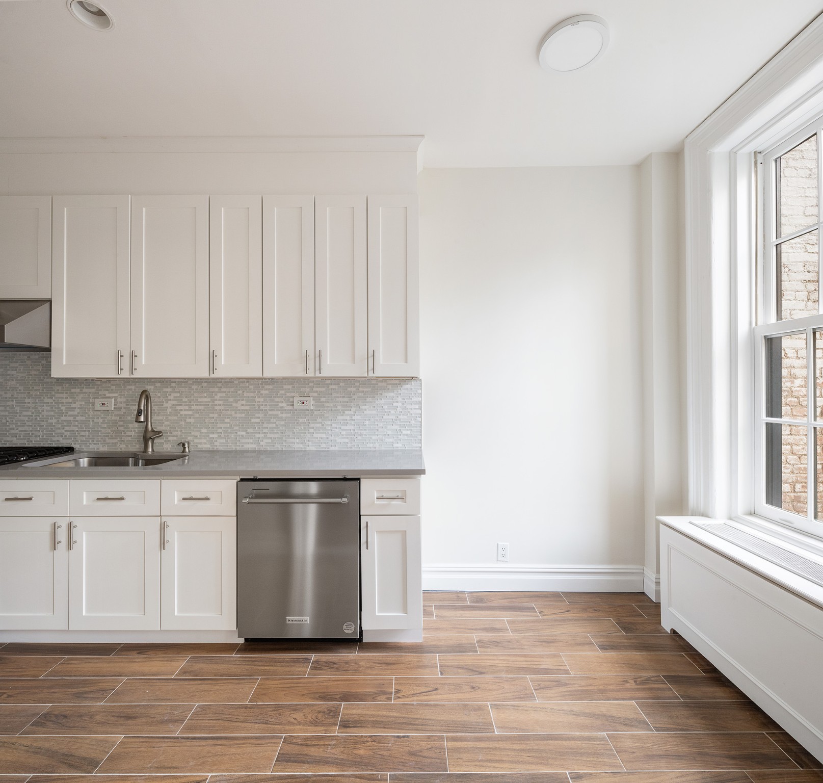 127 East 69th Street, Unit 4 Manhattan, NY 10021 - Photo 6 of 17 a white kitchen with granite countertop a stove a sink and white cabinets with wooden floor