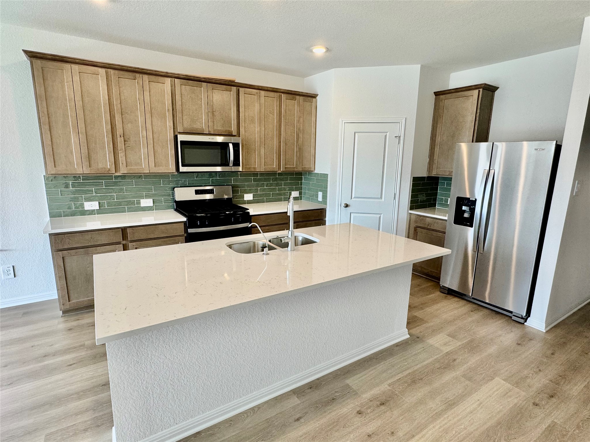 137 Boondoggle Ridge Cedar Creek, TX 78612 - Photo 2 of 7 Kitchen with appliances with stainless steel finishes, light stone countertops, a kitchen island with sink, backsplash, and light wood finished floors