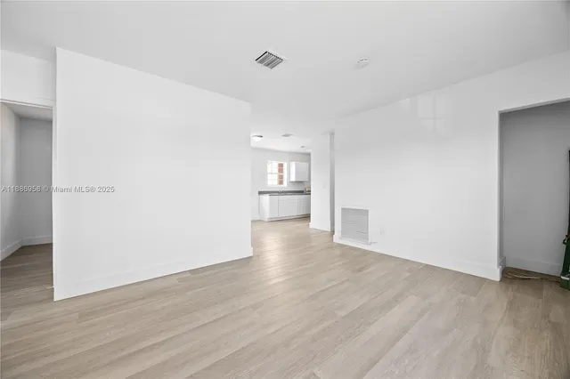 a view of empty room with wooden floor and kitchen