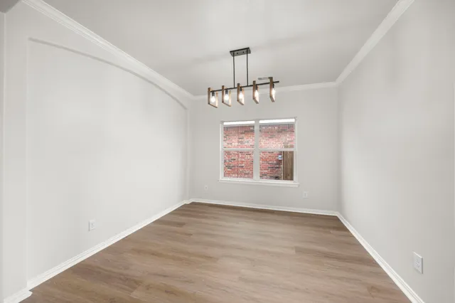 an empty room with wooden floor chandelier and windows