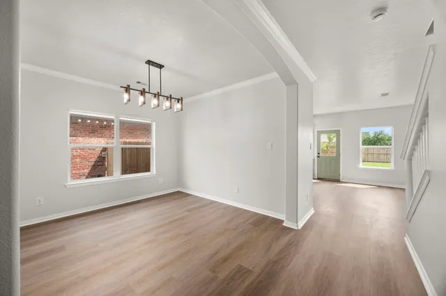 an empty room with wooden floor chandelier and windows