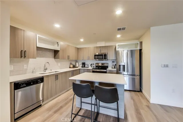 a kitchen with stainless steel appliances granite countertop a stove top oven a sink dishwasher a refrigerator and a dining table with wooden floor