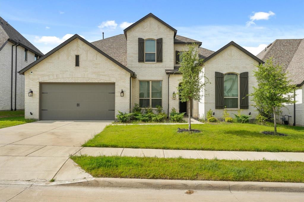 French country inspired facade with brick siding, a front yard, driveway, and a garage