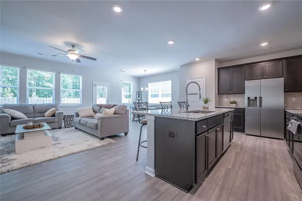 a kitchen with stainless steel appliances granite countertop a refrigerator a sink dishwasher a oven and a dining table with wooden floor
