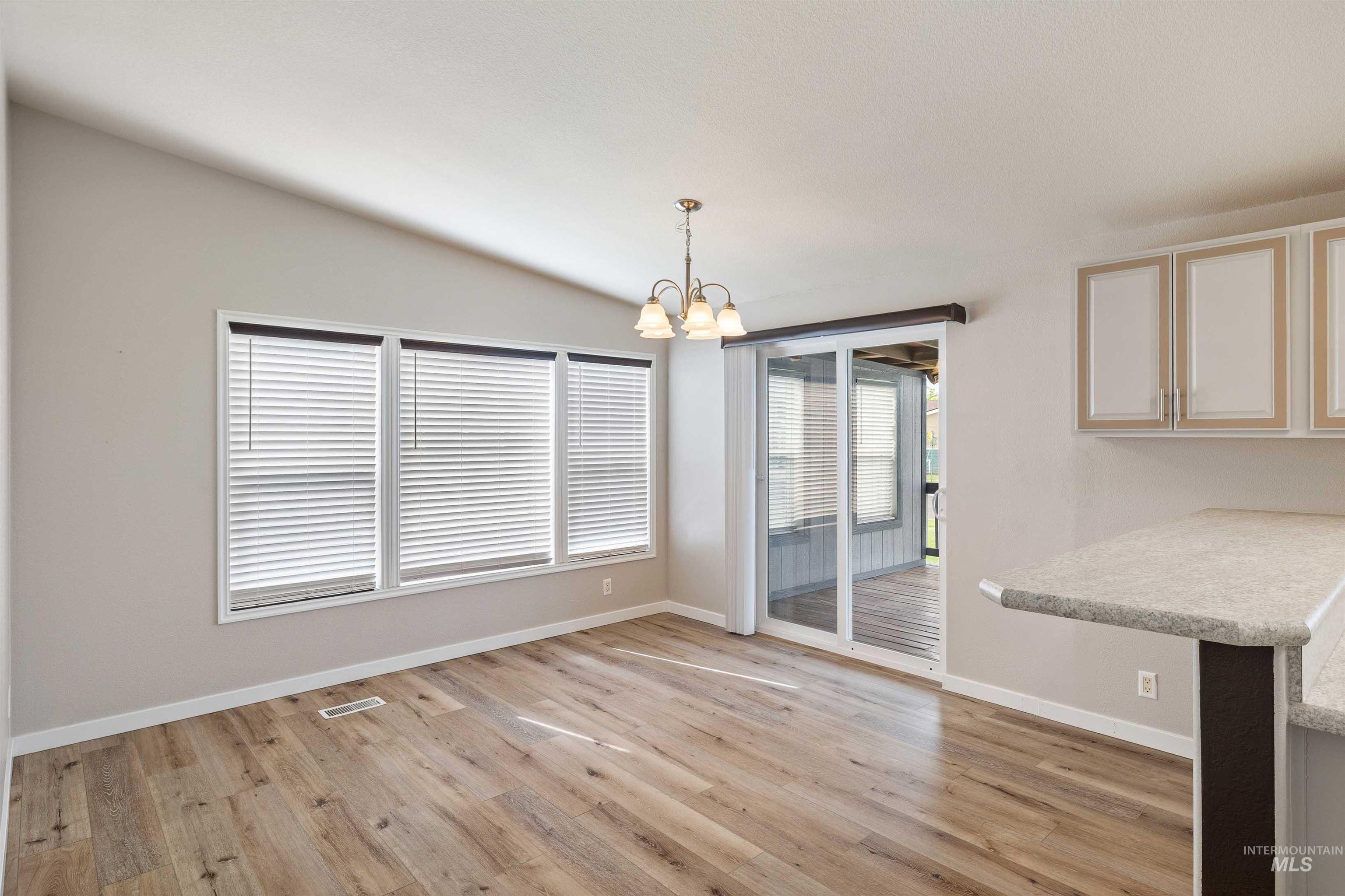 910 Moonglo, Unit 80 Buhl, ID 83316 - Photo 11 of 25 Spacious room featuring wood-finish flooring, a vaulted ceiling, and a multi-light chandelier