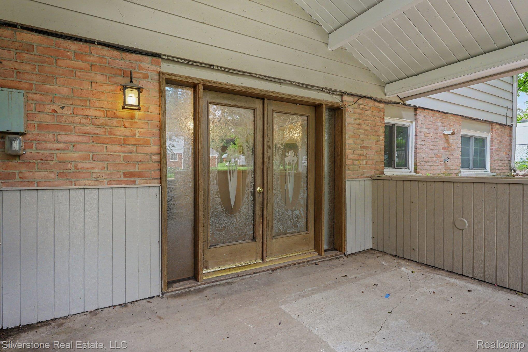 547 Reed Street Northville, MI 48167 - Photo 15 of 38 Covered concrete patio entrance featuring a brick wall with vertical paneling, ornate glass double doors, a side light, and an exterior wall lantern