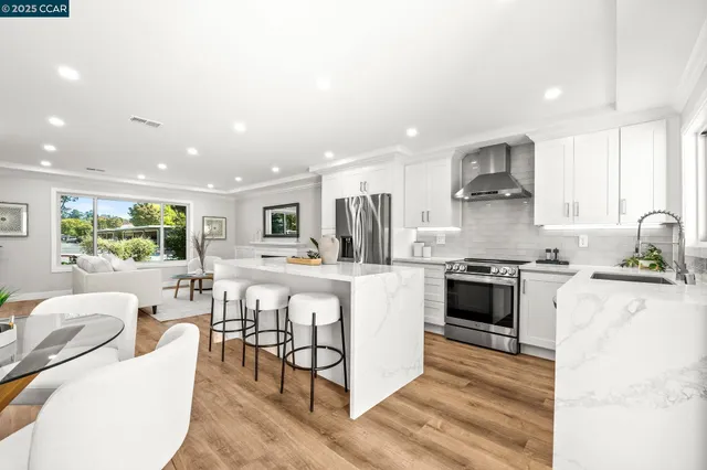 a kitchen with stainless steel appliances kitchen island granite countertop a stove top oven a sink a dining table and chairs with wooden floor