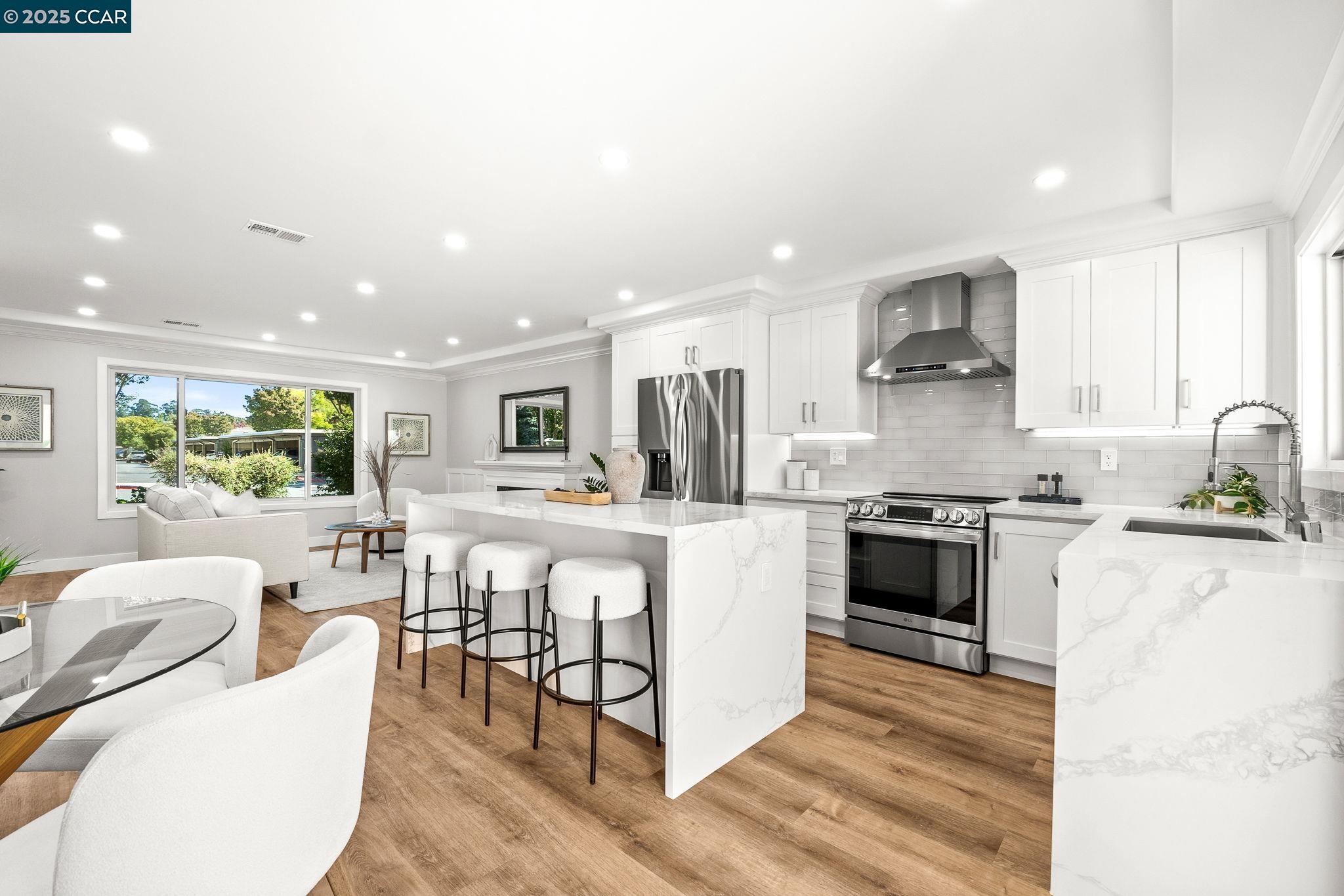 a kitchen with stainless steel appliances kitchen island granite countertop a stove top oven a sink a dining table and chairs with wooden floor