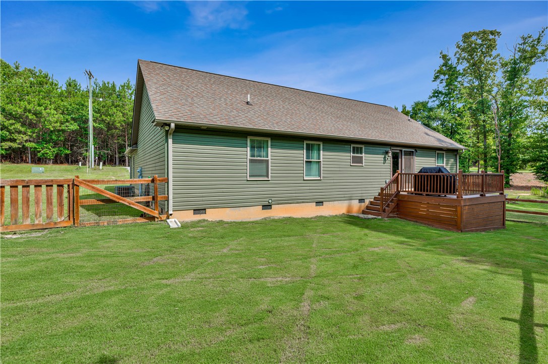 842 Conneross Road Townville, SC 29689 - Photo 28 of 34 A deep green vinyl-sided home presents a wooden back deck and fenced yard, all set against a backdrop of mature trees.