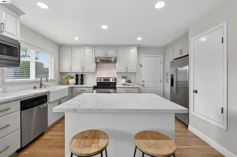 a large kitchen with kitchen island granite countertop a stove a sink a refrigerator and white cabinets with wooden floor