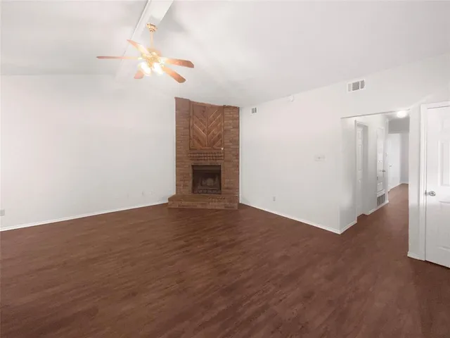 a view of an empty room with wooden floor and a fireplace