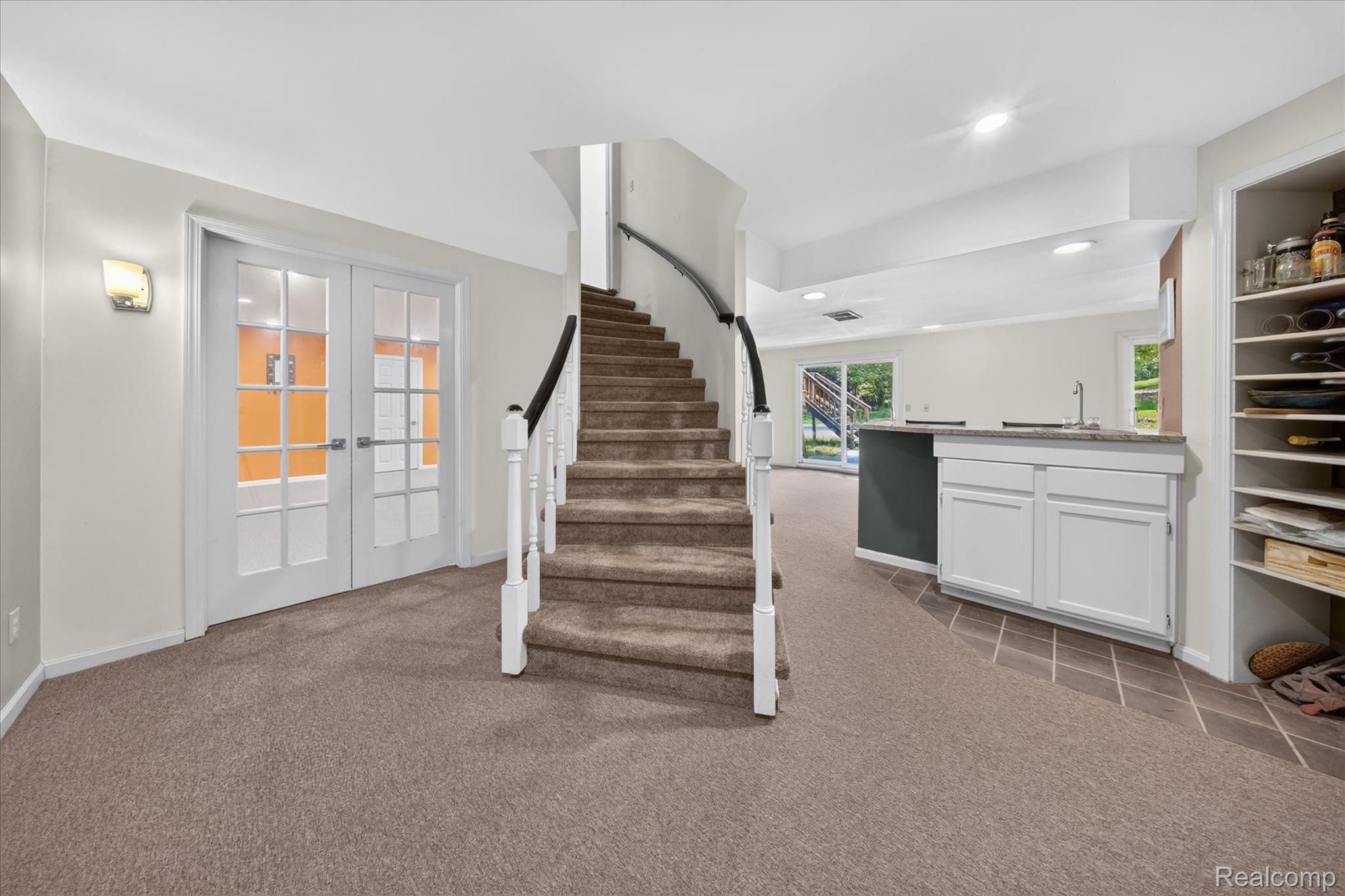 8114 Chilson Road Pinckney, MI 48169 - Photo 18 of 32 Carpeted staircase with white balusters and dark wood handrail, leading to a lower level featuring French doors, a built-in wet bar with white cabinetry, and recessed lighting