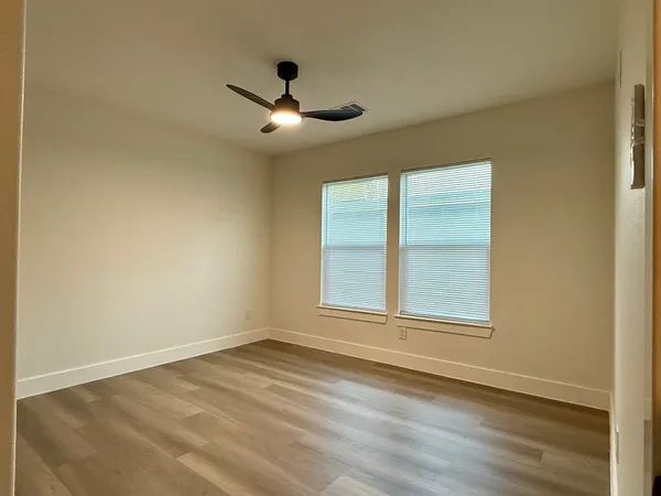 an empty room with wooden floor fan and windows