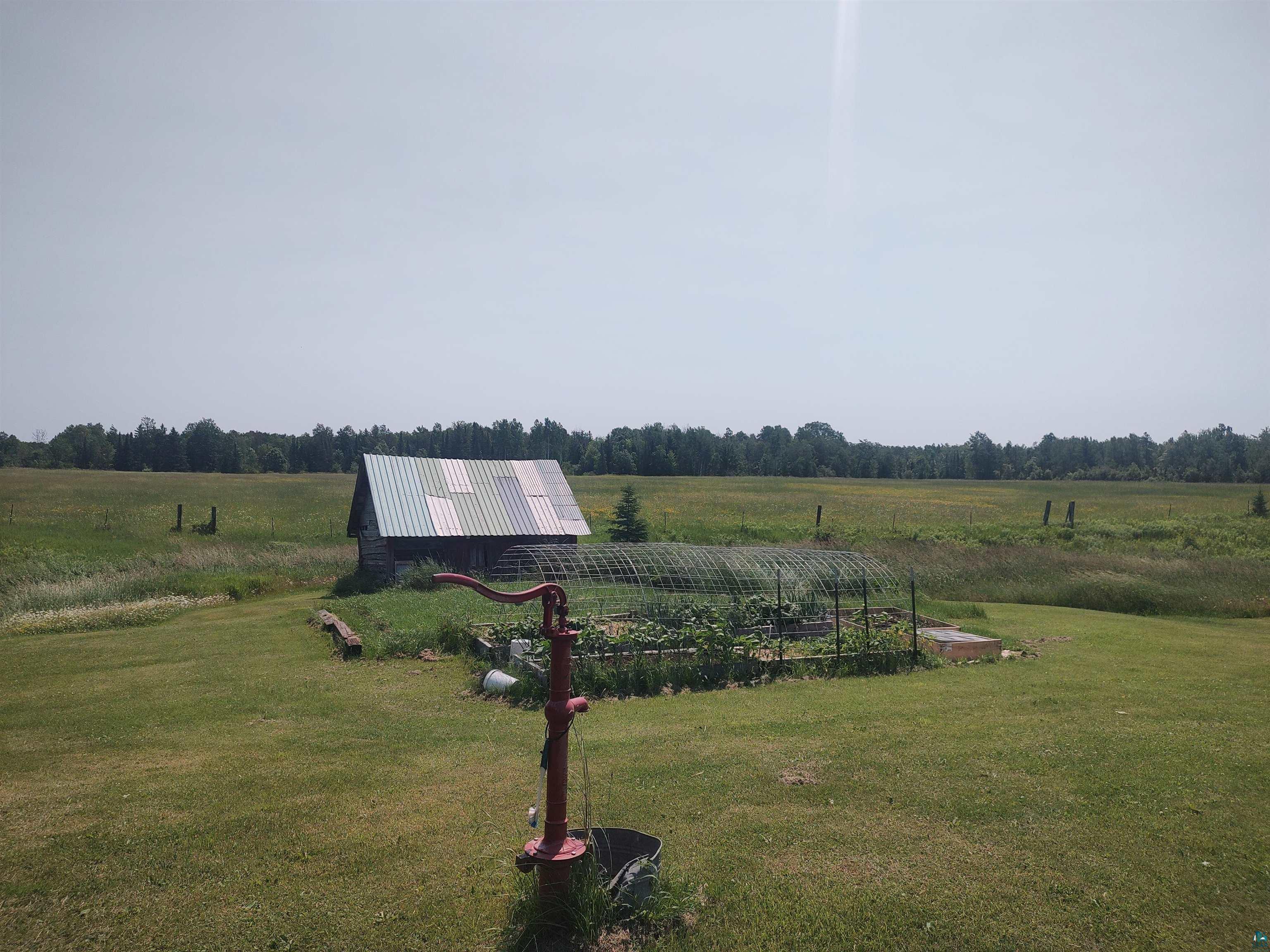 2585 Hautala Road Iron River, WI 54847 - Photo 23 of 28 Expansive green lawn featuring a red hand pump, a fenced garden area, and a rustic outbuilding with a metal roof