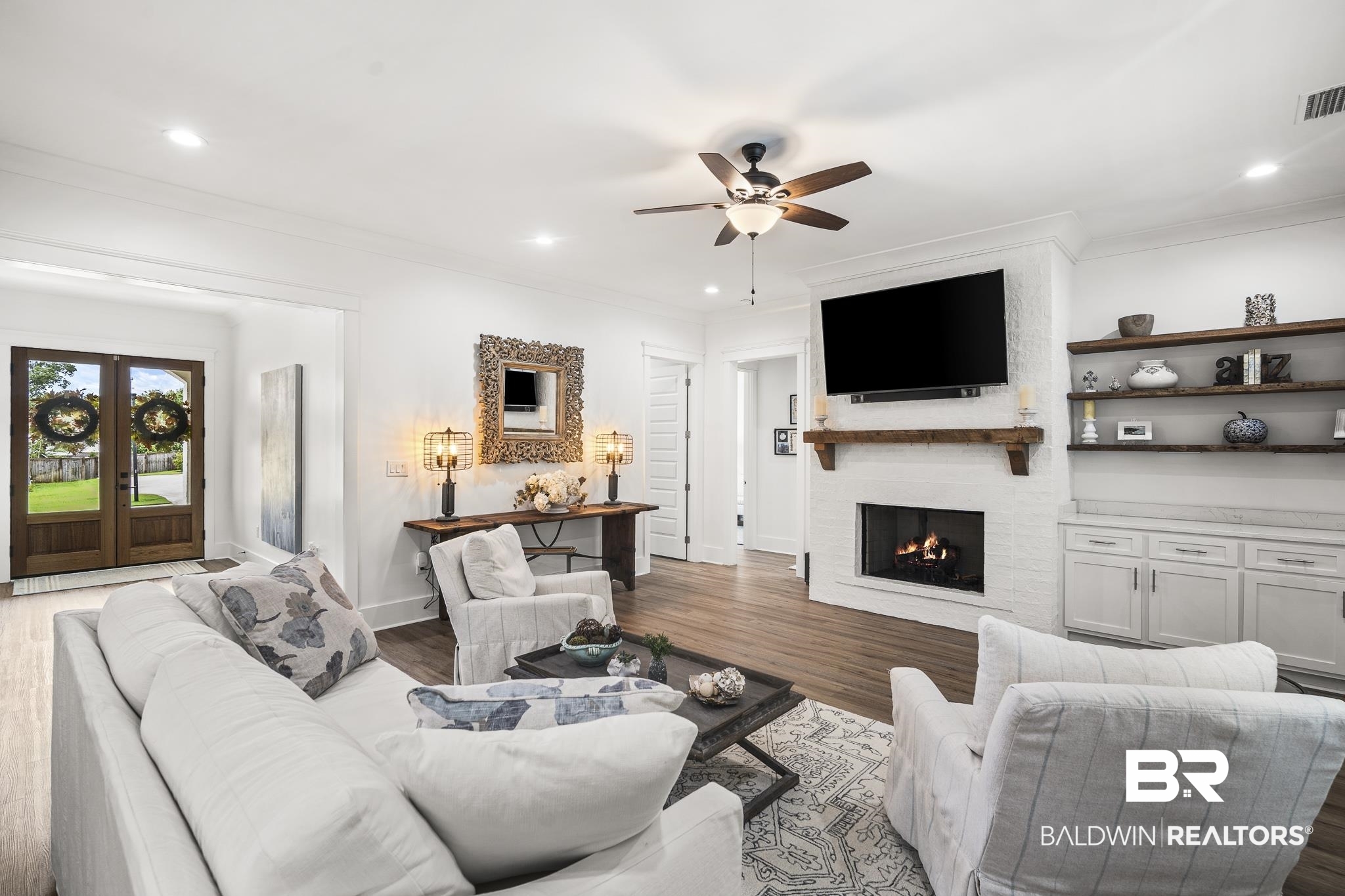 21702 Pillars Street Fairhope, AL 36532 - Photo 8 of 54 Living area featuring wood-finish flooring, a white brick fireplace with a wood mantel, built-in cabinetry with open shelving, and a ceiling fan