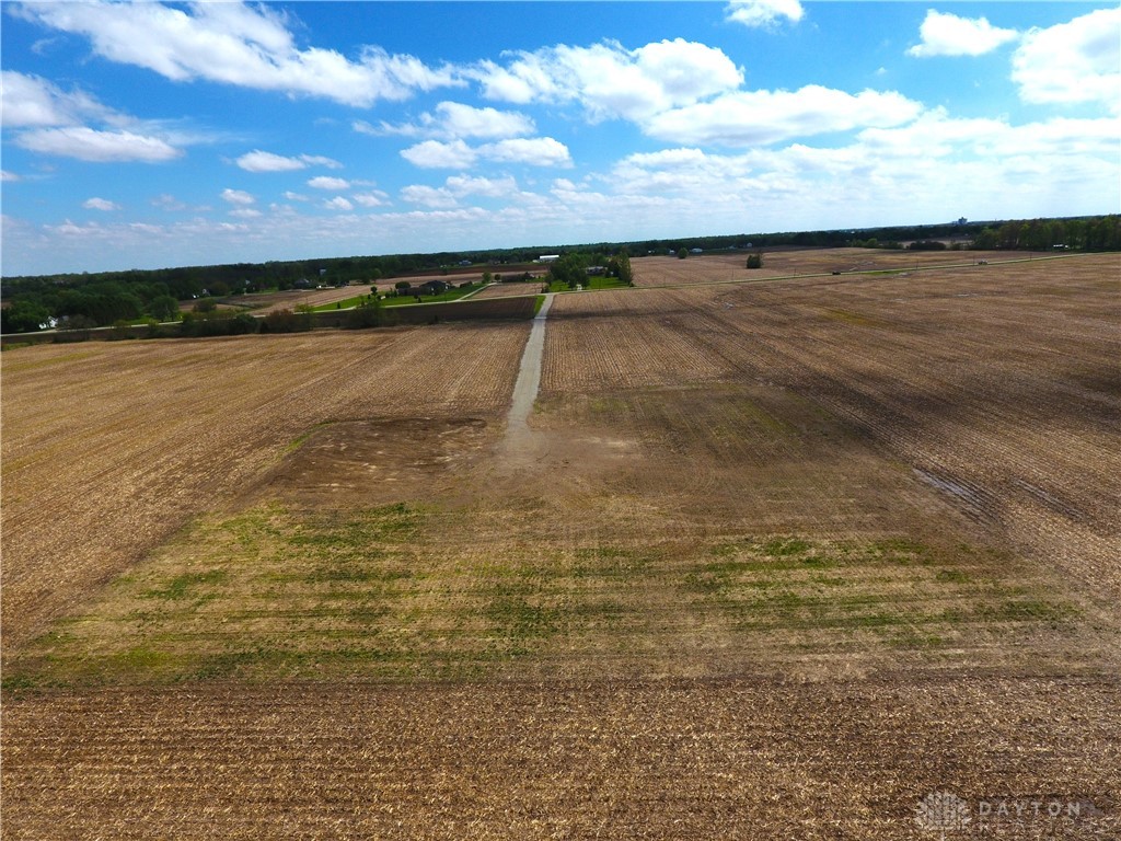 6468 Requarth Road Greenville, OH 45331 - Photo 2 of 4 Expansive farmland offers a tranquil setting with distant trees under a bright, cloud-filled sky.