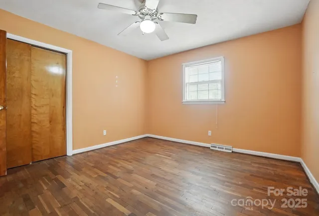 an empty room with wooden floor fan and windows