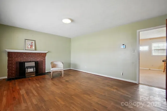 a view of an empty room with wooden floor and a fireplace