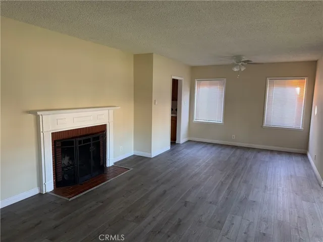 a view of an empty room with wooden floor fireplace and a window