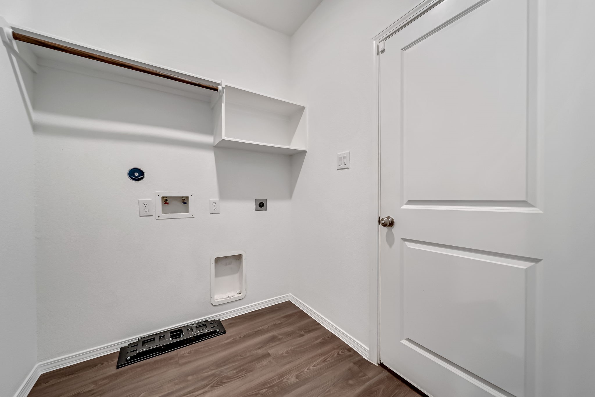 2847 Mistygate Court Conroe, TX 77301 - Photo 18 of 27 This is a laundry room with hookups for a washer and dryer. It features white walls, a wooden shelf with a hanging rod, and a door with a modern design. The room has wood-like flooring and is well-lit, providing a clean and functional space for laundry needs.