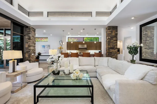 a living room with furniture a rug kitchen view and a large window