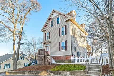 a view of a white house next to a yard with big trees