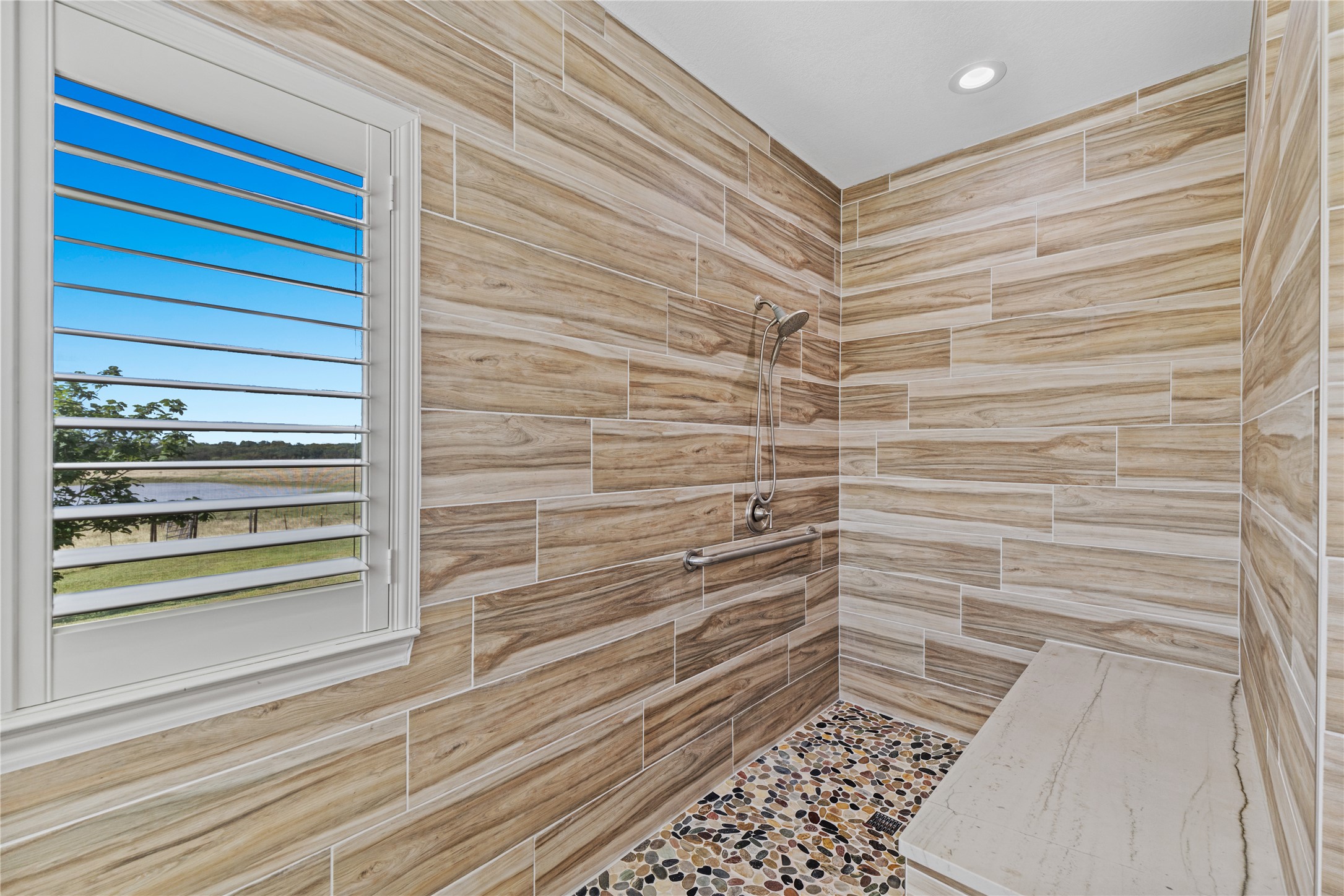 20145 Janak Road Coupland, TX 78615 - Photo 17 of 40 A spacious, accessible shower features wood-look tile, pebble flooring, and a window with a peaceful view.