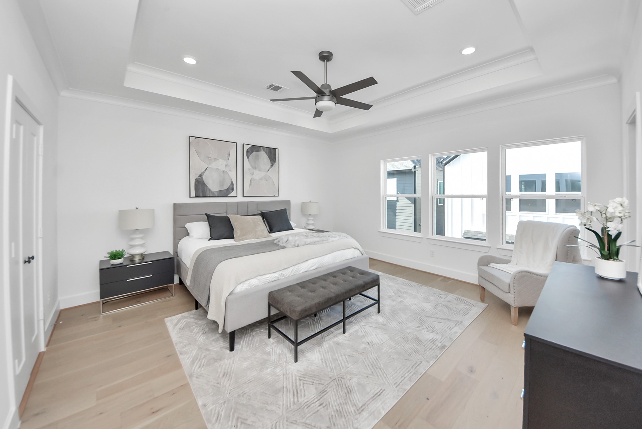 925 Fisher Street, Unit E Houston, TX 77018 - Photo 20 of 47 This spacious bedroom offers a serene retreat with a modern design, a large bed, and stylish furnishings. Natural light streams through multiple windows, highlighting the cozy seating area, ceiling fan, and light wood flooring for a bright, relaxing atmosphere.