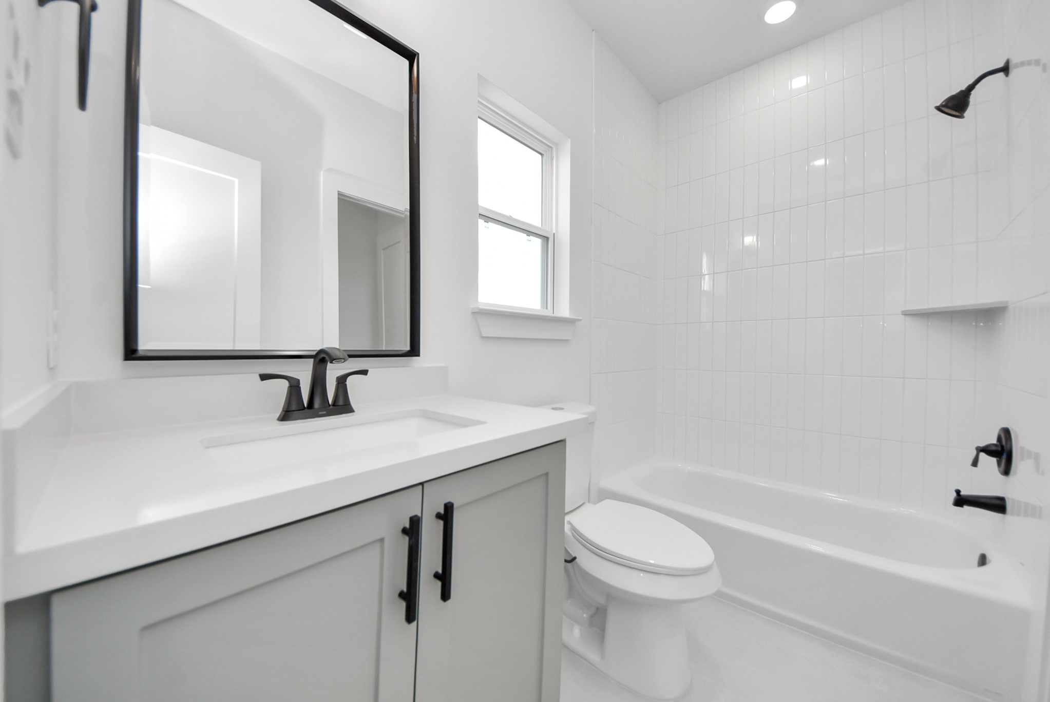 925 Fisher Street, Unit E Houston, TX 77018 - Photo 32 of 47 This modern bathroom features a sleek vanity with a large mirror, a bathtub surrounded by white tile, and a window that brings in natural light, creating a bright and welcoming atmosphere.