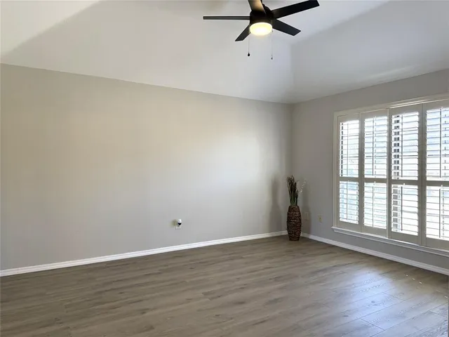 an empty room with wooden floor fan and windows