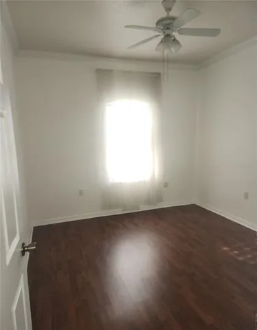 an empty room with wooden floor fan and windows