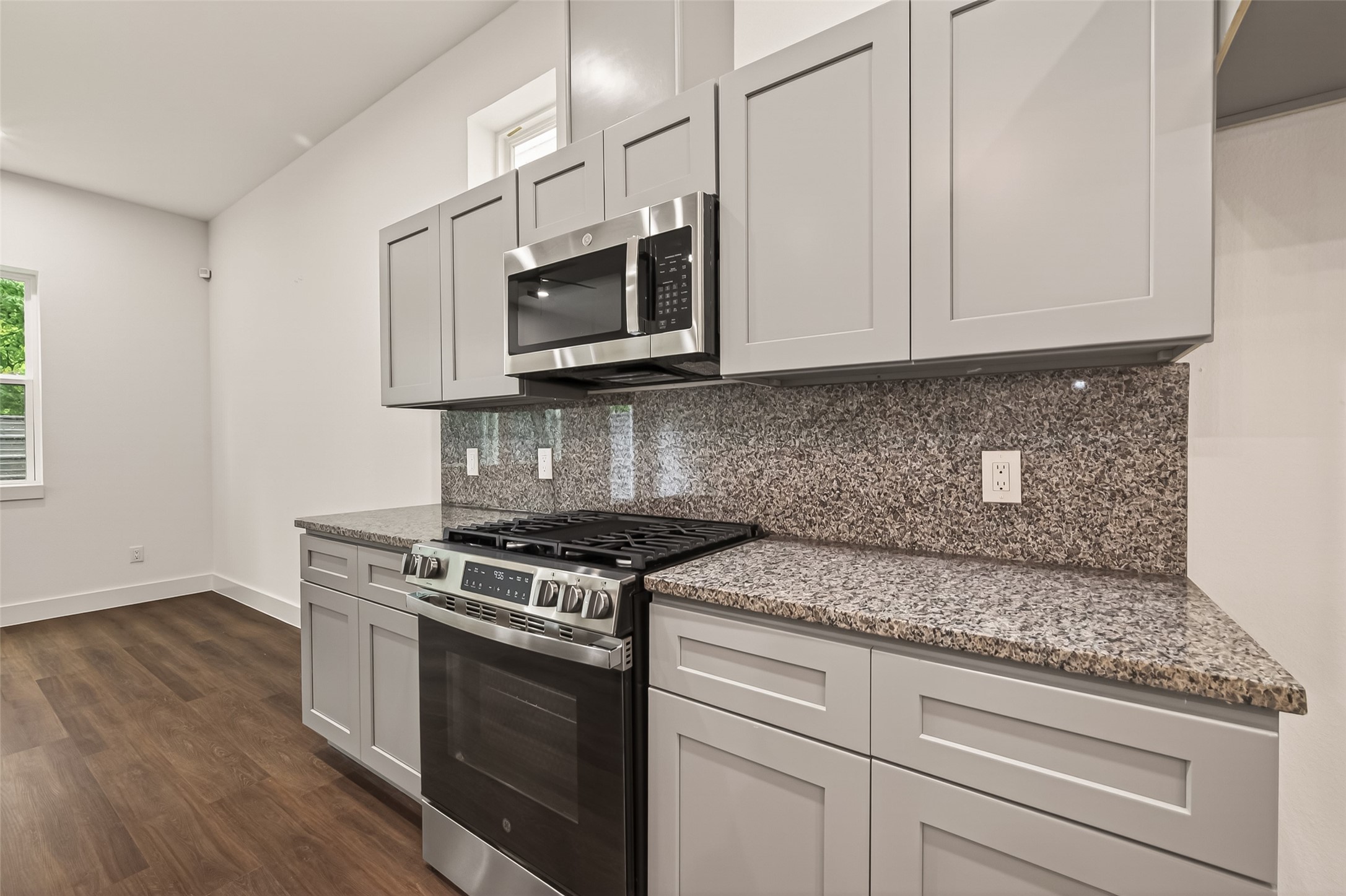 6808 Madrid Street Houston, TX 77021 - Photo 13 of 31 Modern kitchen with sleek gray cabinets, stainless steel appliances, and a granite countertop. The room features a gas stove and microwave, with ample storage and a warm wood floor.