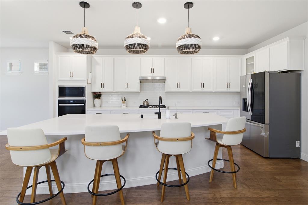7416 Sequoia Rdg Road Little Elm, TX 76227 - Photo 20 of 37 Kitchen featuring a large island with seating, white shaker cabinetry, stainless steel appliances, wood-finish flooring, and pendant lighting