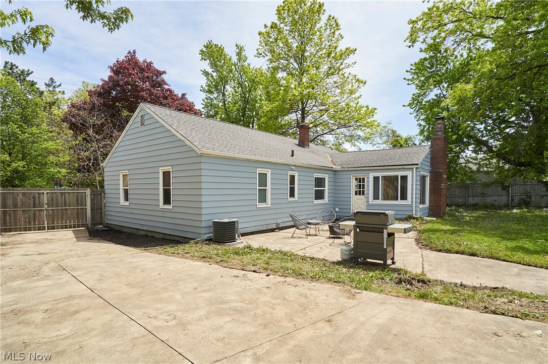 780 Bates Road Rocky River, OH 44116 - Photo 29 of 35 Rear exterior featuring light blue siding, a stone chimney, multiple windows with white trim, and a concrete patio