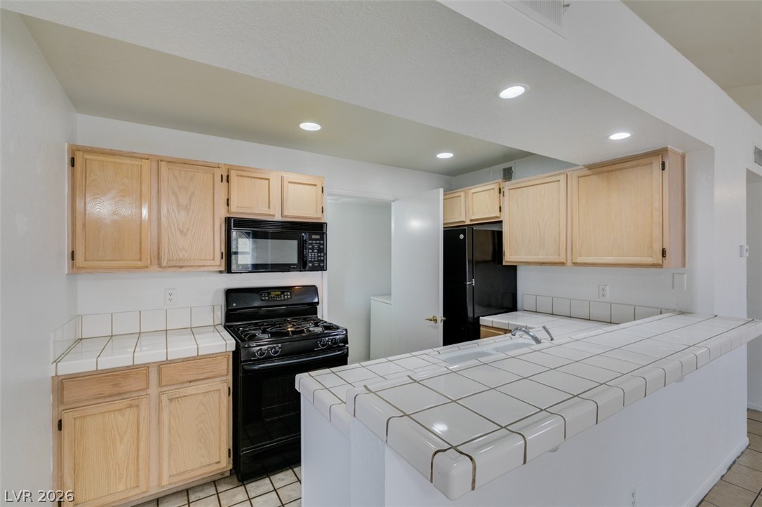 7570 West Flamingo Road, Unit 252 Las Vegas, NV 89147 - Photo 23 of 44 A functional kitchen features light wood cabinetry, tiled countertops, and contemporary black appliances.