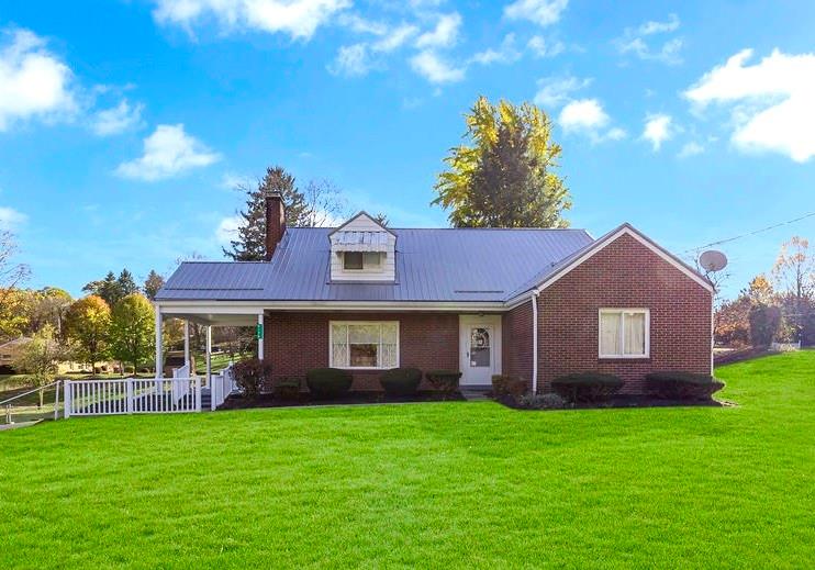 a view of a brick house with a big yard potted plants and large tree