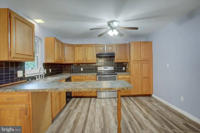 a view of a kitchen with kitchen island granite countertop wooden floor stainless steel appliances a sink and cabinets