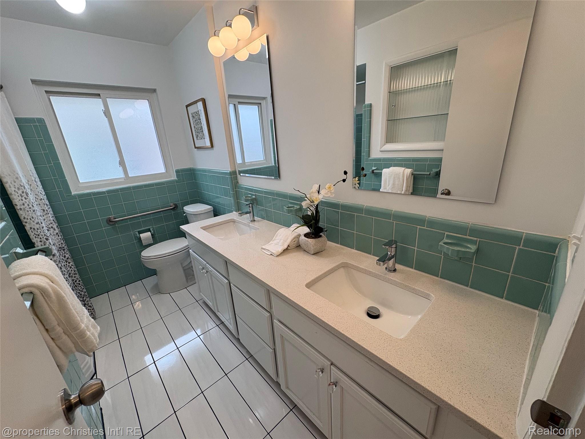 17330 Beverly Road Franklin, MI 48025 - Photo 13 of 24 Full bathroom featuring double vanity, light tile patterned floors, tile walls, curtained shower, and a wainscoted wall