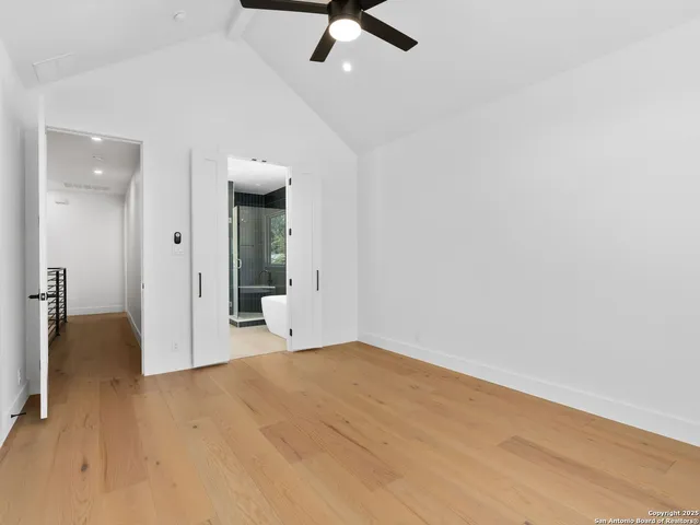 an empty room with chandelier fan and kitchen view