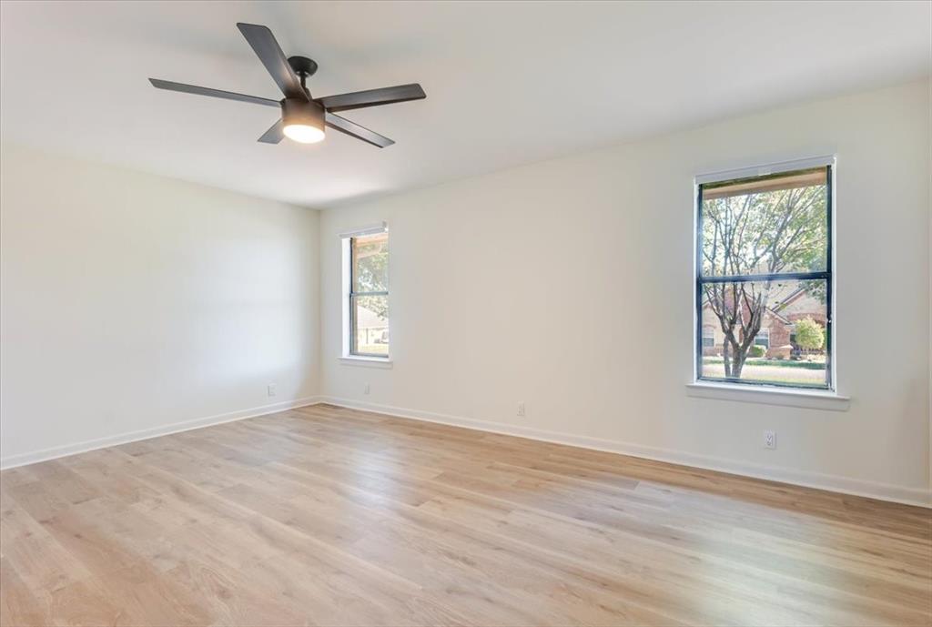 8105 Ravenswood Road Granbury, TX 76049 - Photo 11 of 28 Light wood-finish flooring, two windows with white trim, and a ceiling fan with integrated lighting