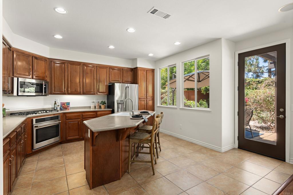 5439 Foxtail Loop Carlsbad, CA 92010 - Photo 14 of 47 a kitchen with kitchen island granite countertop wooden cabinets a stove a sink a oven with a dining table and chairs