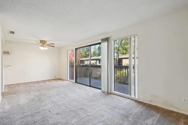 an empty room with chandelier fan and windows
